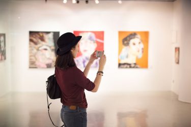 Girl in a museum taking a picture of an artwork.